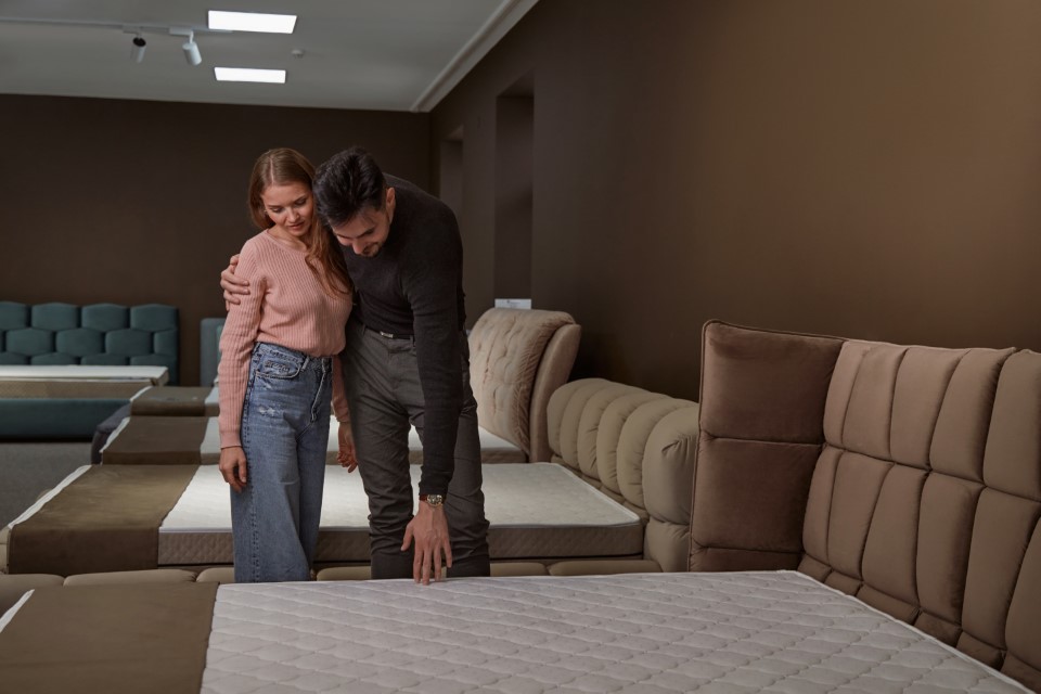 Para testuje materac w salonie, kobieta leży, a mężczyzna sprawdza, jak materiał reaguje na nacisk.